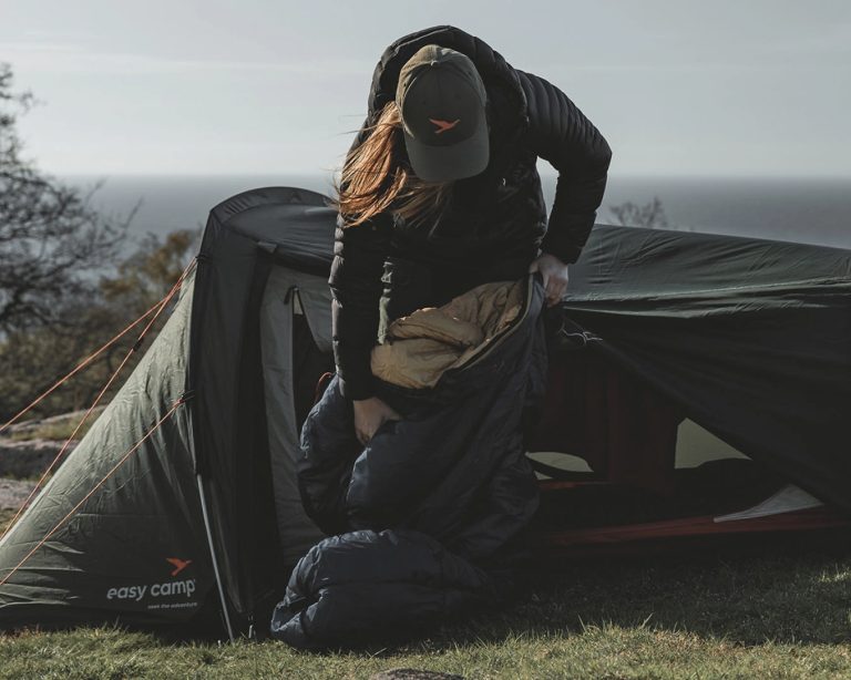 Easy Camp Falcon II Mummy -1°C 1 Easy Camp Falcon II Mummy -1°C Saco de Dormir é desempacotado por uma mulher em frente a uma tenda