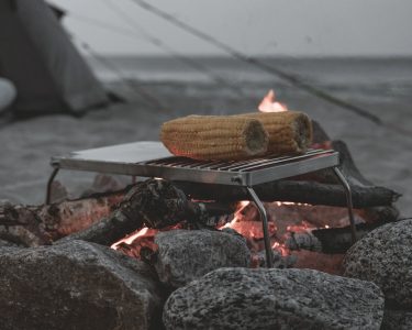 O Campfire Grill da marca easy camp dobrável, à luz de uma fogueira com alimentos grelhados
